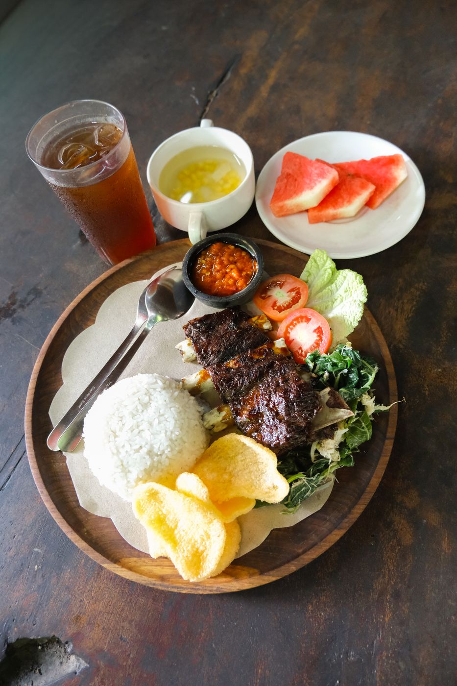 Grilled pork ribs served with rice, sambal matah, crackers, and fresh fruit